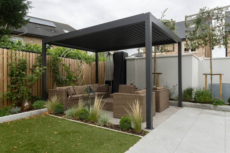 A grey metal pergola with a louvred roof over garden seating